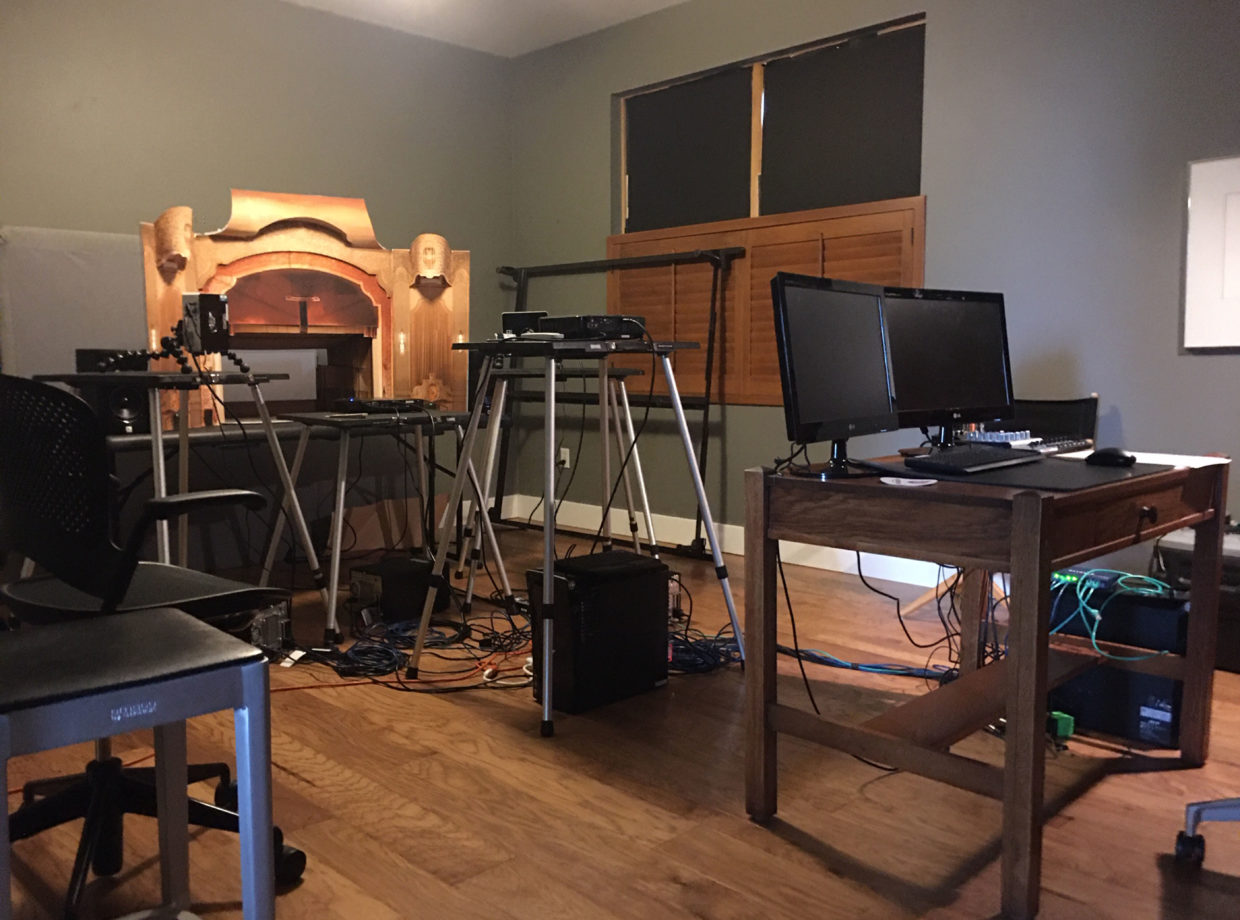 View of artist's studio, with computers on a desk, many projectors, stands, and wires, and a scale model of the Arlene Schnitzer Concert Hall in the far corner